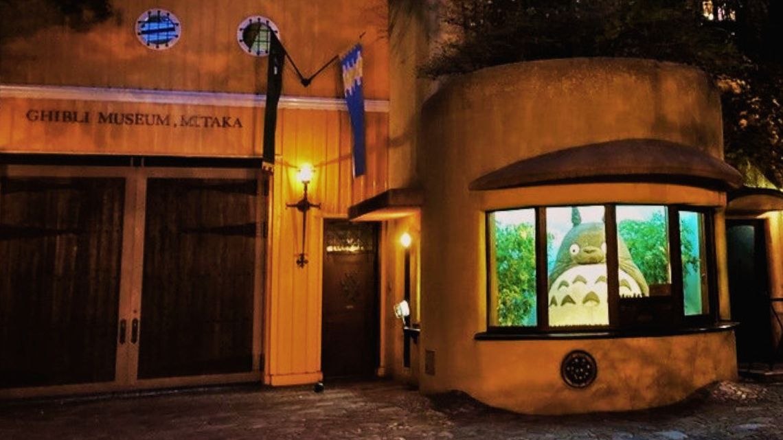 The outside of the Ghibli Museum at night with a lit window showing the statue of the anime character Totoro
