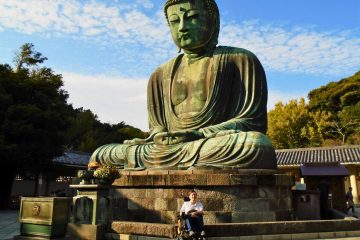 Justin in his power wheelchair sitting in front of the Giant Buddha of Kamakura on a sunny day