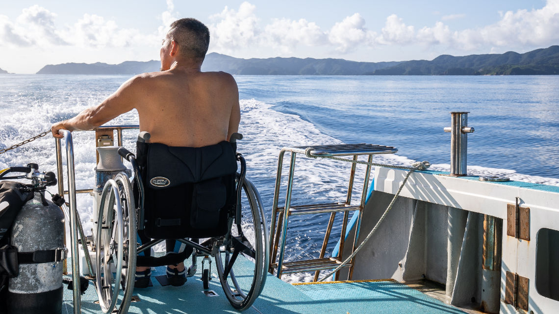 Man in a wheelchair looking out to sea from the back of a boat