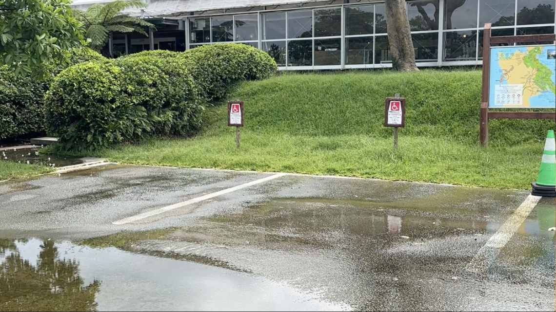 Empty parking spots at Bios no Oka with disabled access signs, wet pavement with puddles, greenery, and a map display in the background.