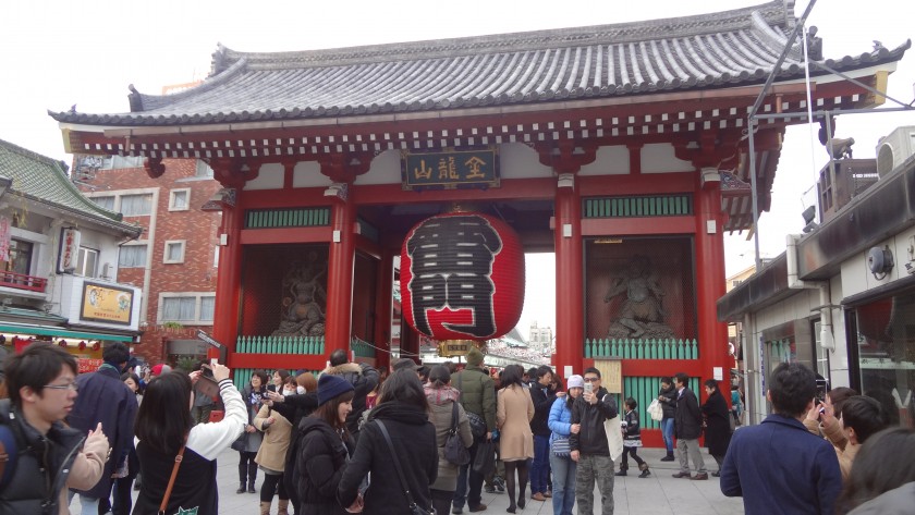 Visitors gather at the Kaminarimon gate of Senso-ji Temple in Tokyo, featuring a large red lantern and traditional statues.