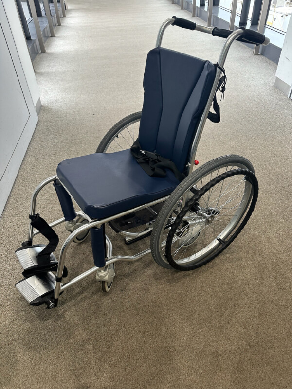 A lightweight aisle wheelchair with large rear wheels, designed for easy airport use, is stationed in a terminal.