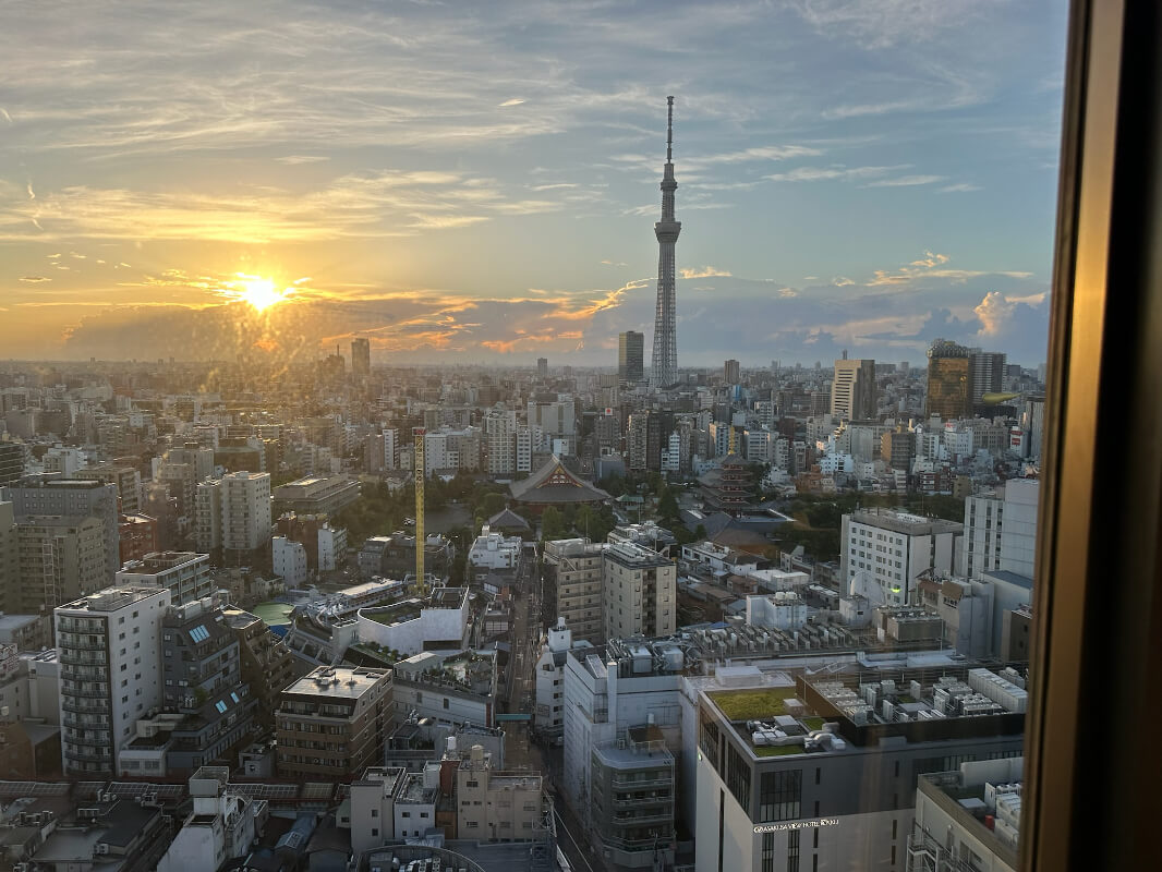 A stunning sunset view of Tokyo from a high-floor hotel room at Asakusa View Hotel, with the iconic Tokyo Skytree standing tall amidst the city's skyline, bathed in golden light.