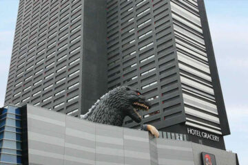 A giant Godzilla head peers over the top of Hotel Gracery in Shinjuku, Tokyo. The life-sized Godzilla replica adds a unique and iconic touch to the city’s skyline, drawing visitors' attention.