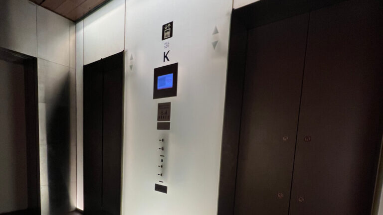 A modern elevator lobby with two black doors, a control panel, a screen display, and soft lighting in a sleek, minimalist design.