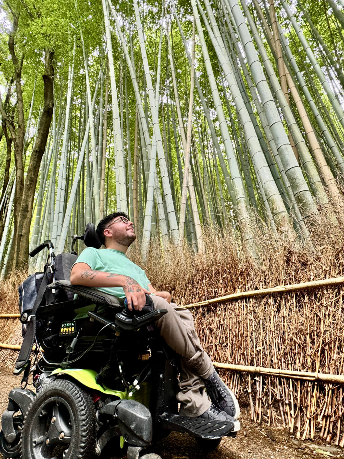 Cory Lee, a wheelchair user, exploring the towering bamboo grove in Arashiyama, Kyoto, surrounded by tall green bamboo and a rustic fence